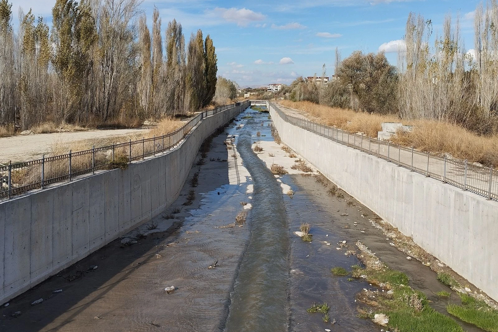 A concrete-lined drainage channel carrying water between protected embankments.
