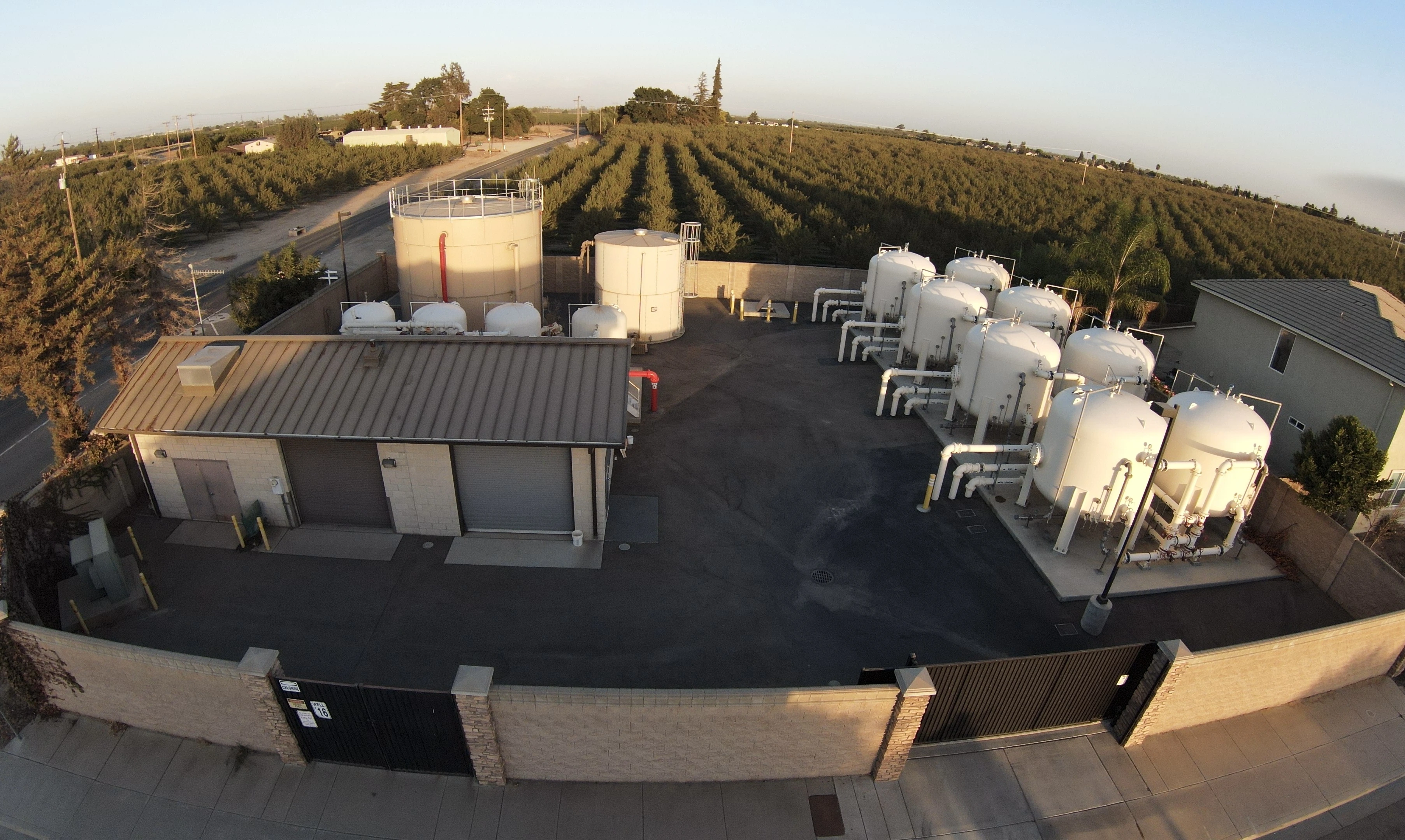Livingston well facility with treatment tanks and piping beside surrounding orchards.