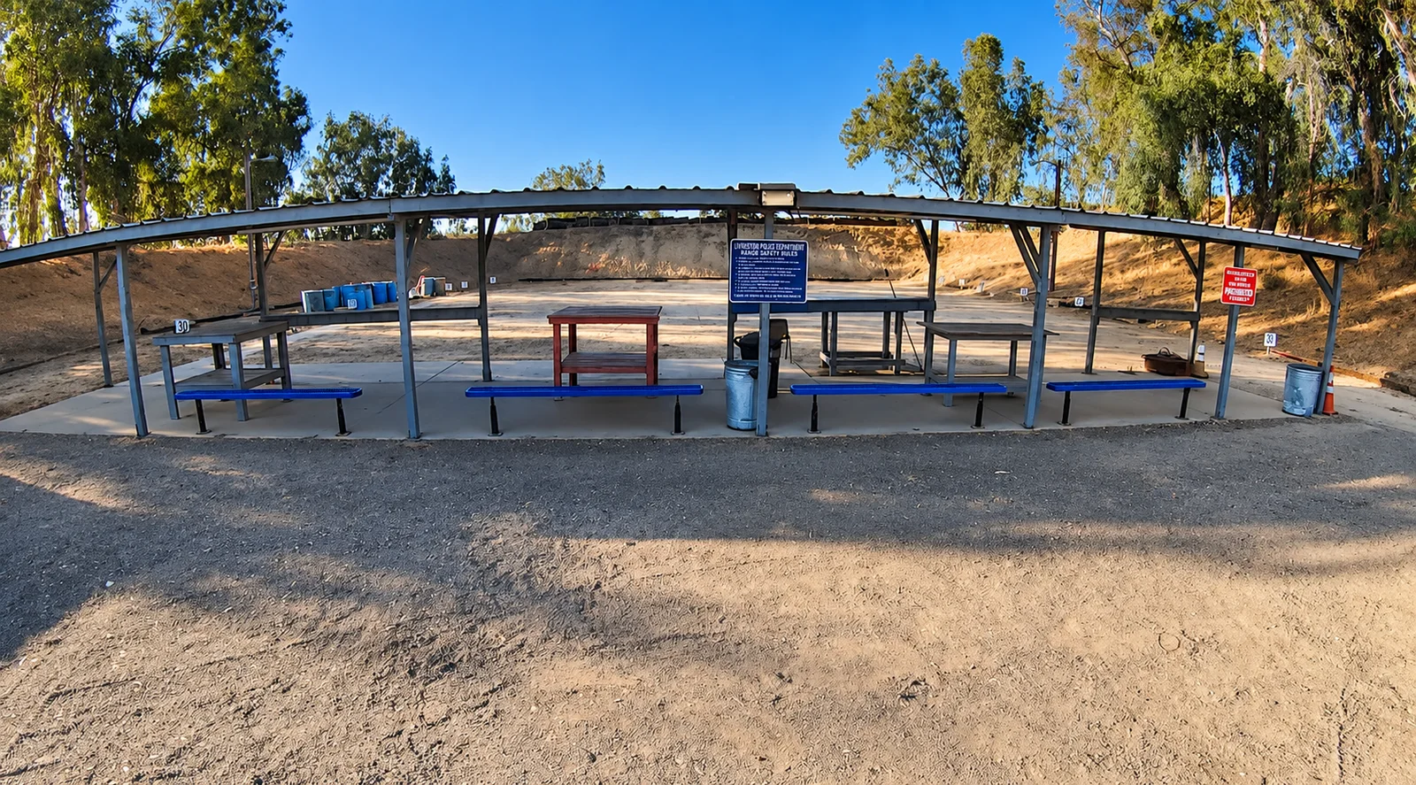 Ground-level view of the Livingston Police Department shooting range, showing the covered firing line, benches, and earthen backstop.